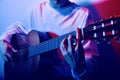 Close-up of fingers on the neck of an acoustic guitar. Muchina plays the guitar in neon. Musician, music, training