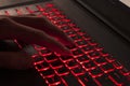 Close up of fingers typing on glowing red backlight keys on a computer keyboard. in the dark. Computer hacker, internet fraud or s