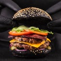Close-up, finishing touch making grilled burger. Chef hands in black gloves are closing top black bun of burger