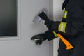 Close-up of a firefighter in protective clothing in front of a metal closed door, breaking with an axe