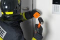Close-up of a firefighter in protective clothing and a hard hat trying to open a door with a sledgehammer and chisel