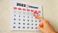 Close-up of the first page of a wall calendar 2022 and a male hand moves a red cursor to the 1st January date