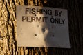 Close up of a fishing by permit only sign attached to a large tree in the winter Royalty Free Stock Photo