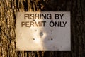 Close up of a fishing by permit only sign attached to a large tree in the winter Royalty Free Stock Photo