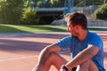 Close-up of a fit man, tired after running sitting on the race track. Determined and concentrated male athlete resting after