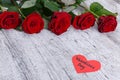 Red roses on a gray wooden background, with a heart with an inscription the day of St. Valentine, a free place for text. Royalty Free Stock Photo