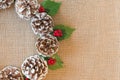 Close-up of flat lay Christmas wreath of pinecones, red berries, and holly leaves on rustic fabric background Royalty Free Stock Photo