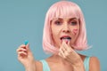 Close up of a flirtatious female model on blue background wearing a pink wig with a candy in mouth. Pretty glamorous