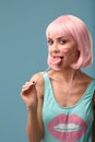 Close up of a flirtatious female model on blue background wearing a pink wig holding different kinds of candies. Pretty