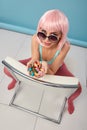 Close up of a flirtatious female model on blue background wearing a pink wig holding different kinds of candies. Pretty