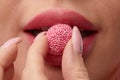 Close up of a flirtatious female model with a candy in mouth. Pretty glamorous woman pink hair charm sweets lifestyle