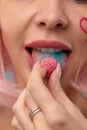 Close up of a flirtatious female model with a candy in mouth. Pretty glamorous woman pink hair charm sweets lifestyle