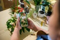 Close-up florist holds smartphone, photographing a bouquet of flowers in wicker basket, created in floral design studio