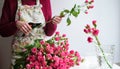 Close-up of a florist woman`s hand in a flower apron cuts the stems of a bouquet of pink roses with shears in a flower shop at