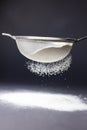 Close-up of flour sifting through sieve on table against black background, copy space