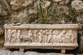 Close-up of a flower pot with a bas-relief depicting people and animals against a stone wall and a green plant.