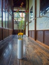 Close up of a flower vase with a yellow flower and red branch at indoor view of hall with a wooden floor, in Kyoto
