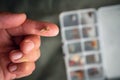 Close up of fly fishing fly on the finger next to box with tied flies. Fly fishing equipment still life