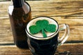 Close-up of the foam of a dark beer with a shiny clover leaf  served in a mug on a wooden table. Royalty Free Stock Photo