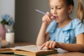 Close-up focus on foreground of thoughtful elementary child school girl doing homework and holding pen against mouth Royalty Free Stock Photo