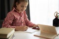 Close up focused little girl using phone studying online, sitting at table at home, serious child holding smartphone Royalty Free Stock Photo