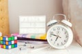 Close up focused white alarm clock with blurred Back to school message hashtag on lightened box, notebooks, rubik`s cube and Royalty Free Stock Photo