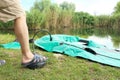 Close-up foot of Caucasian young man pumping green rubber boat in the morning for fishing on lake shore outdoors Royalty Free Stock Photo