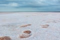 Close-up footsteps on salt pink lake, cloudy sky