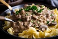 Close-up of a fork twirling strands of homemade egg noodles covered in creamy beef stroganoff sauce, garnished with fresh chives