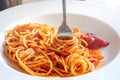 A close up fork is wrapped in Italian spaghetti pasta in a white plate with ketchup sauce
