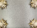 Close up four 4 gold Christmas tree toys with sharp tips,stars,in corners on shiny shimmering silver sequined background