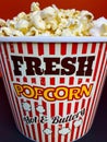 Close up fresh buttery popcorn in a stripped red and white bowl on red background Royalty Free Stock Photo