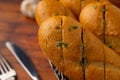 Close-up of fresh cheese garlic bread cut in half with aromatic herbs on a wooden board on a wooden table with sliced garlic in