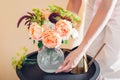 Close up of fresh english roses Lady of Shallott. Woman puts vase with bouquet of orange flowers on table at home. Royalty Free Stock Photo