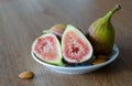 Close-up of fresh figs with one slised ripe fig and three almond nuts lying on white plate on a wooden table background Royalty Free Stock Photo