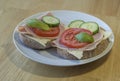 close up fresh home made rye bread sandwich with ham cheese sliced cucumbre tomatoes and basil leaves on white plate on wooden ta Royalty Free Stock Photo