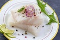 Close up Fresh raw cod fish fillet on a plate with parsley and lemon isolated on grey slate background Royalty Free Stock Photo