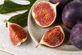 Close-up of fresh ripe fig fruits on a beige ceramic plate and a green leaf over a white wood table. Sweet fruits and berries. Royalty Free Stock Photo