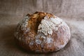 Close up of fresh round loaf of healthy whole grain bread on brown jute burlap fabric background with white flour on top. top view Royalty Free Stock Photo