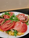 Close up of fresh salad featuring sliced tomatoes, ham, arugula, and corn, served on white plate, creating vibrant and Royalty Free Stock Photo