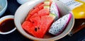 Close up fresh sliced of watermelon and dragon fruit in plate with bottle of orange juice on black wooden table. Royalty Free Stock Photo