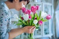 Close up fresh spring pink and white tulips bouquet in a vase and blurred woman enjoying flowers smell with closed eyes in light Royalty Free Stock Photo
