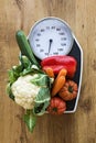 Fresh vegetables on kitchen scale over wood background. Royalty Free Stock Photo