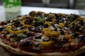 Close-up of a freshly baked pizza with meat, onions, mushrooms, and green and yellow peppers on a wooden table Royalty Free Stock Photo