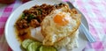 Close up fried egg or yolk on top with white rice, sliced cucumber and minced pork basil in white plate on colorful table