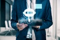 Close up and front view of businessman hand using cellphone with glowing robot head on blurry office background. Chat bot and