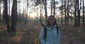 Close up front view of charming happy female model walking in autumn forest among green pines at sunset. Young woman enjoying autu