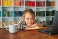 Close-up front view of cheerful attractive pupil child school girl lying at table with laptop and paper workbook Royalty Free Stock Photo