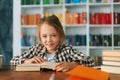 Close-up front view of cheerful pupil school girl kid doing homework reading paper book sitting at table in children