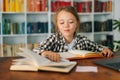 Close-up front view of cute pupil school girl kid doing homework reading paper book sitting at table in light children Royalty Free Stock Photo